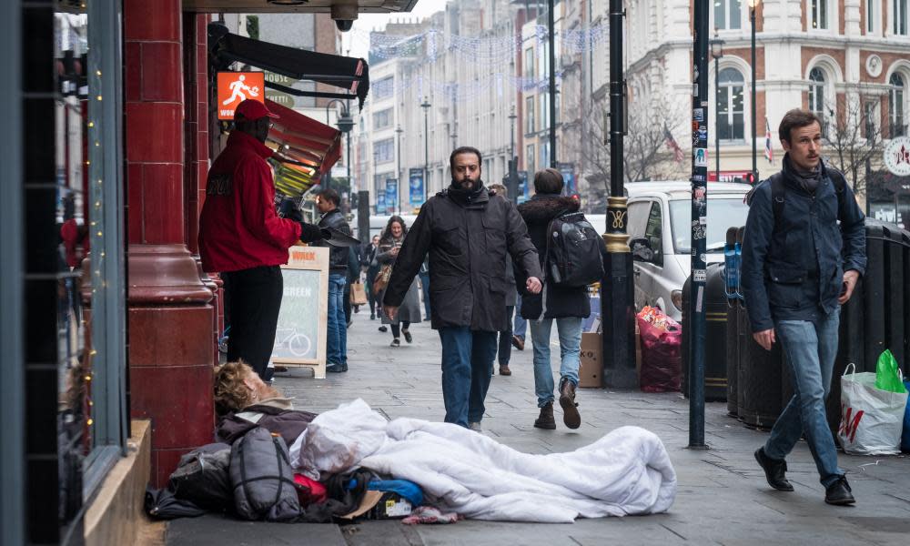 People walk past a homeless man sleeping outside Leicester Square underground station in London last week