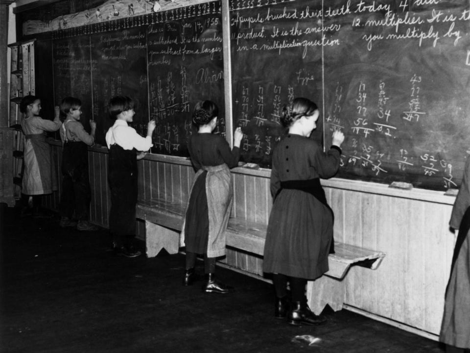 Amish schoolchildren do some sums on a blackboard. All grades are taught in the same room and take it in turns to use the board in 1956,