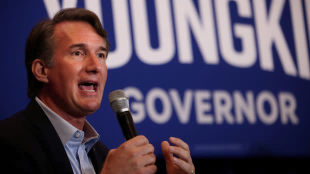 Glenn Youngkin speaks with a microphone in front of a blue sign that says "Youngkin for Governor."