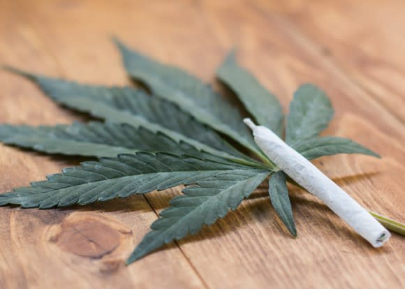 A cannabis joint lying atop a cannabis leaf on a table.