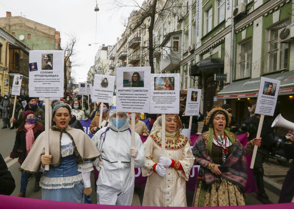 Activists dressed as women historical figures hold portraits of outstanding women in history at a rally on the occasion of the International Women's Day in Kyiv, Ukraine, Monday, March 8, 2021. Millions across the globe are marking International Women's Day by demanding a gender-balanced world amid persistent salary gap, violence and widespread inequality. (AP Photo/Efrem Lukatsky)