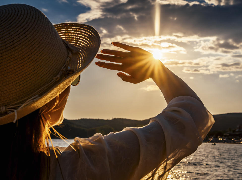 Young woman blocking sun with hands on the beach during sunset. UPF is used to determine protection from UV rays in clothing. (Getty)