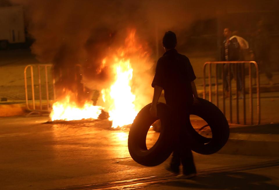 A Sunni protestor carries tires as a fire set by Sunni protesters burns on a major roadway between Beirut and the capital's southern suburbs, a Hezbollah stronghold, to show support for residents of the Sunni town of Arsal, in Beirut, Lebanon, Tuesday, March 18, 2014. Gunmen from Lebanon's militant Hezbollah group and local Shiite Muslim residents tightened their blockade of a Sunni town of Arsal near the Syrian border Tuesday, sparking concerns that thousands of Syrian refugees stranded in the area could be cut off from humanitarian aid. (AP Photo/Hussein Malla)