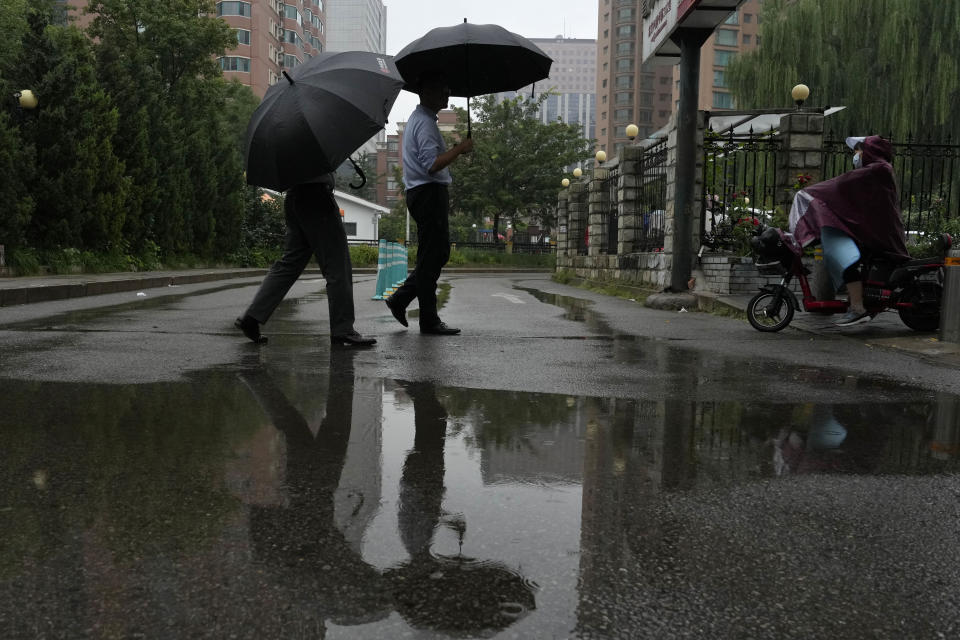 Residents walk with umbrellas near a puddle during a rainy day in Beijing, Thursday, Aug. 18, 2022. Some were killed with others missing after a flash flood in western China Thursday, as China faces both summer rains and severe heat and drought in different parts of the country. (AP Photo/Ng Han Guan)