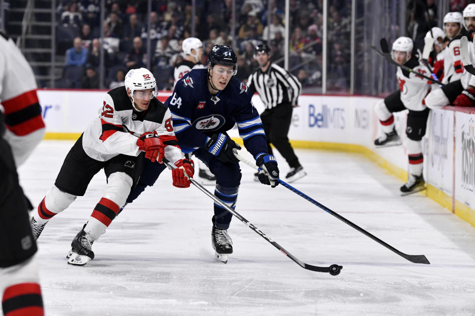 New Jersey Devils' Tomas Nosek (92) and Winnipeg Jets' Logan Stanley (64) vie for the puck during the second period of an NHL hockey game Tuesday, Nov. 14, 2023, in Winnipeg, Manitoba. (Fred Greenslade/The Canadian Press via AP)