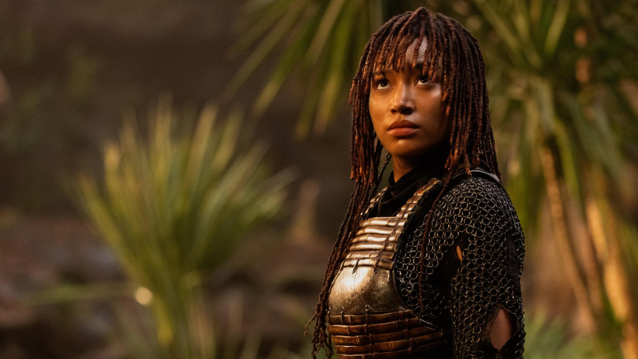  A young woman with braids stands with blurry palm trees in the background. 