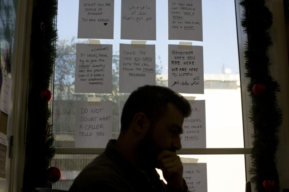 In this Monday, Dec. 23, 2019 photo, words of encouragement are taped to a window next to Bassem, a volunteer, as he waits for calls at at Lebanon's Embrace, a mental health organization operating the national suicide prevention helpline in Beirut. Lebanon is entering its third month of protests, the economic pinch is hurting everyone, and the government is paralyzed. So people are resorting to what they've done in previous crises: They rely on each other, not the state. (AP Photo/Maya Alleruzzo)