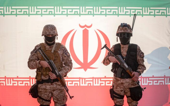 Two Islamic Revolutionary Guard Corps personnel pose in front of a flag