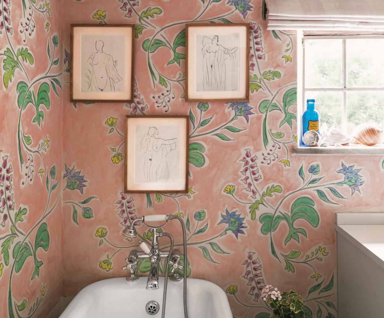  A bathroom with a bright pink botanical wallpaper and three sketched on the wall. 