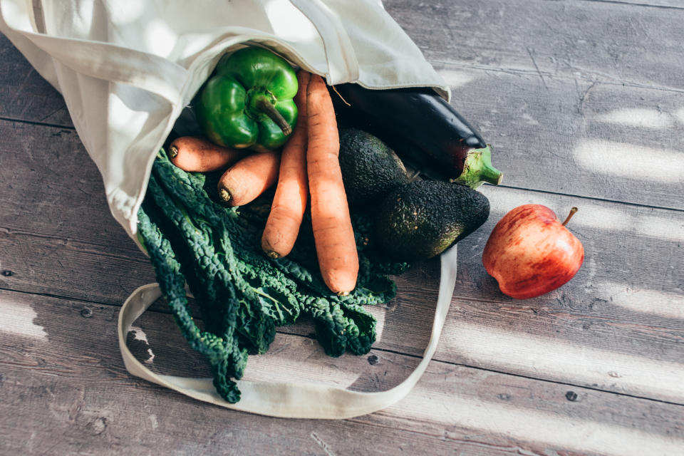 Close-up shot of a tote bag with various vegetables on a wooden table.