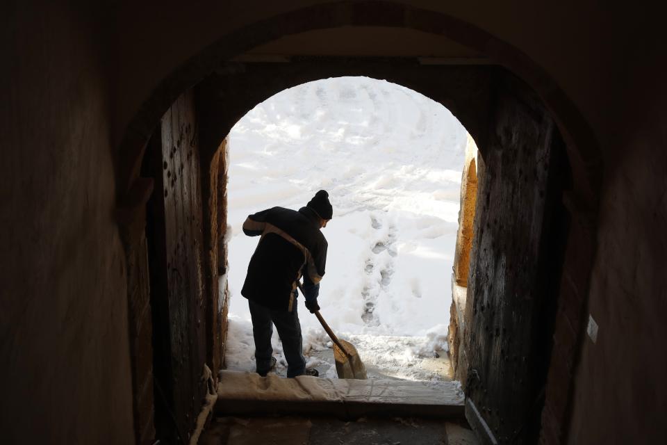A worker clears the snow-covered entrance of Penteli Monastery in northern Athens, Tuesday, Jan. 8, 2019. Schools will remain closed across many parts of the country as a new cold weather front brings freezing temperatures and heavy snowfall. (AP Photo/Thanassis Stavrakis)