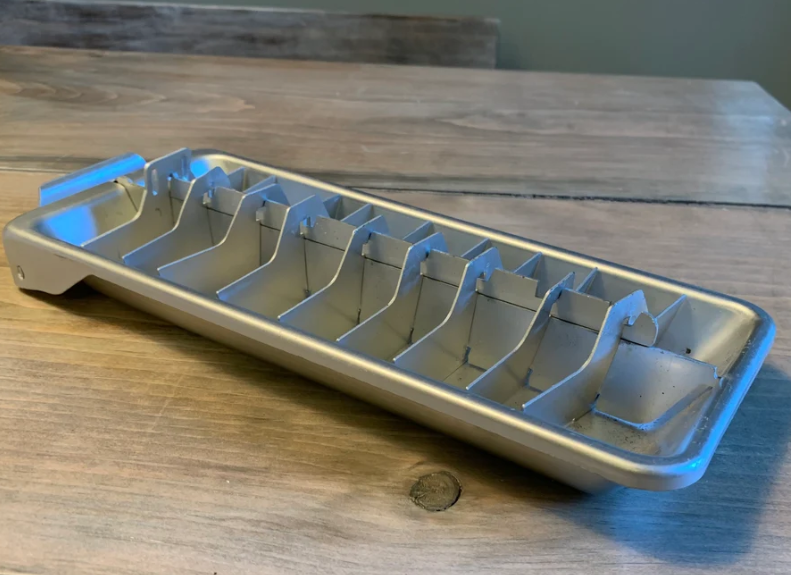 Metal ice cube tray with a handle and dividers on a wooden surface