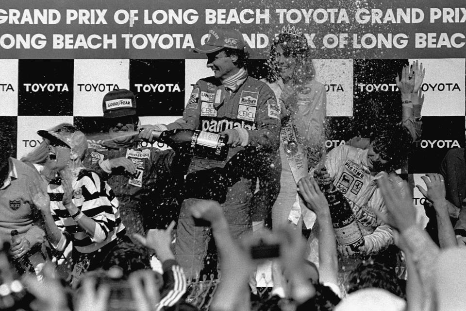 FILE - Two-time Formula 1 world champion Niki Lauda, center, sprays champagne over well wishers around the winner circle at the Grand Prix circuit in Long Beach, Calif., in this April 5, 1982, file photo. Lauda, driving for Team McLaren, won the race, finishing ahead of Team Williams driver Keke Rosberg, left, of Finland, second, and Canadian Gilles Villeneuve, right, who finished third driving for Ferrari. The Grand Prix of Long Beach opens 17 months after the pandemic ended the crown jewel’s streak as one of the longest continuously-running street events in racing. (AP Photo/FIle)