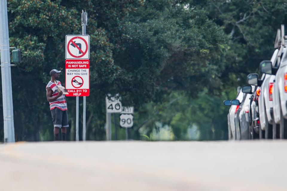 A man holding a sign asking for money as new street signs installed warning motorist that panhandling is not safe. Wednesday, July 28, 2021.