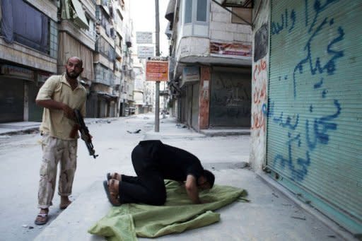 A Syrian rebel stands guard next to a comrade praying during a short break of heavy fighting in the Salaheddin district of Aleppo on August 3. Syria's prime minister Riad Hijab has joined the anti-regime revolt and fled abroad, in what Washington and the opposition hailed as a major blow to President Bashar al-Assad