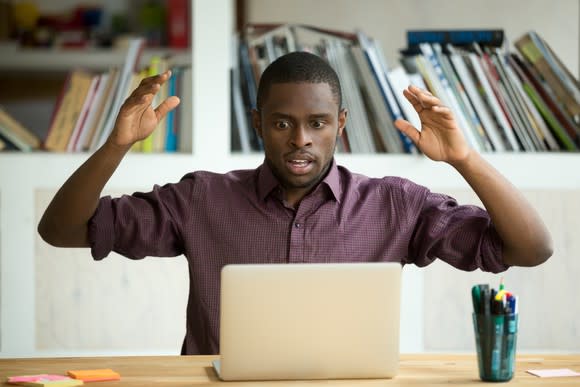 young man with arms raised, looking shocked at what he sees on his laptop