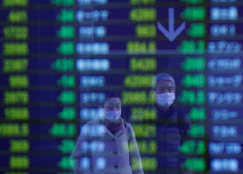 FILE PHOTO: Passersby wearing protective face masks, following an outbreak of the coronavirus, are reflected on a screen displaying stock prices outside a brokerage in Tokyo