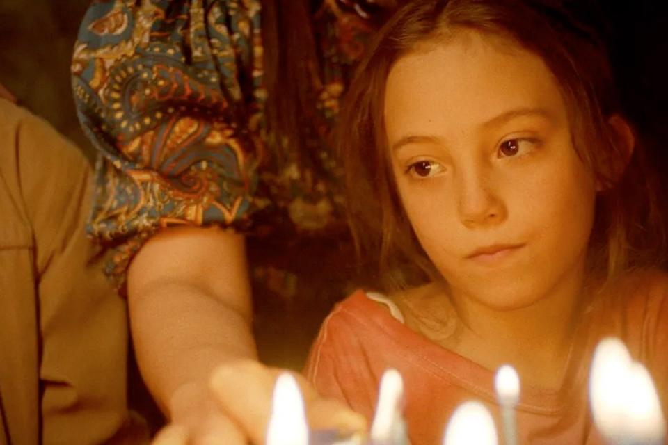 A young girl illuminated by the candles on a cake looks very sadly off to the side. 