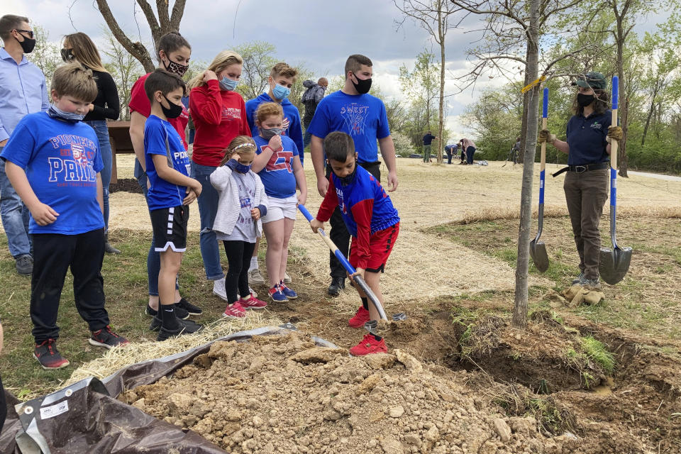 Educators and schoolchildren plant one of the trees at the dedication of Ohio's COVID-19 Pandemic Memorial Grove at Great Seal State Park near Chillicothe, Ohio, on April 30, 2021. A memorial grove to COVID-19 victims has been planted and governors and lawmakers elsewhere are pursuing similar permanent remembrances. (AP Photo/Julie Carr Smyth)