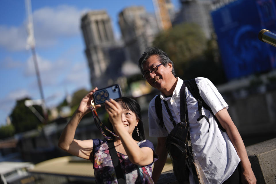 Japanese tourists Ken Kito and his wife snap a selfie with the under-construction Notre-Dame Cathedral in the background, ahead of the 2024 Summer Olympics, Monday, July 22, 2024, in Paris, France. (AP Photo/Rebecca Blackwell)