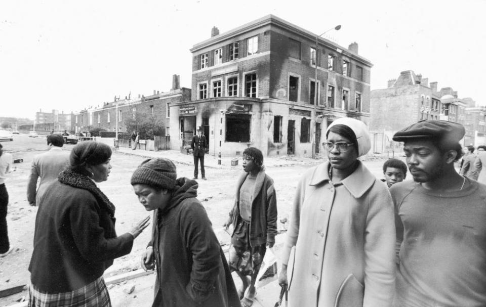 Local residents walk past a burned-out pub in Brixton after a second night of rioting in the area, 13 April 1981.