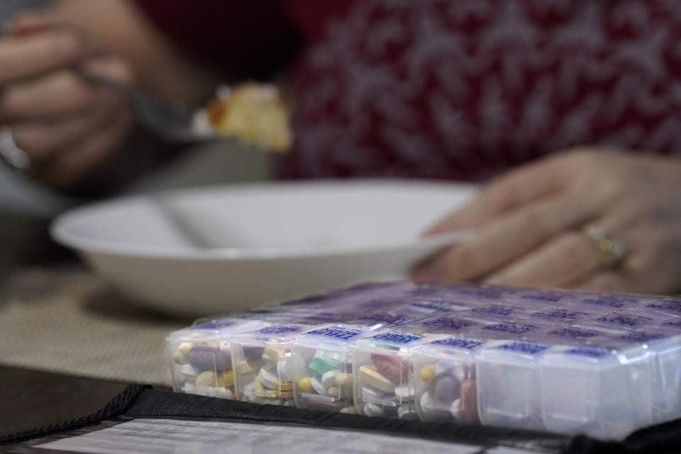 Her regimen of daily pills sit in a container as Kari Wegg finishes her breakfast in her home in Westfield, Ind., on Tuesday, March 23, 2021. (AP Photo/Charles Rex Arbogast)