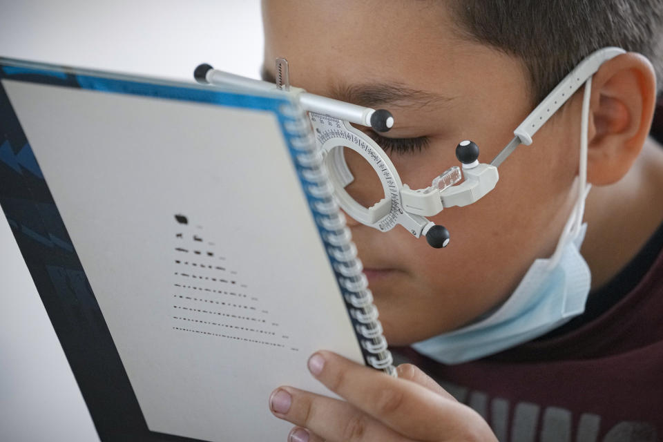 A boy reads a text with testing glasses during an eyesight examination performed by volunteer ophthalmologists working with the humanitarian organization Casa Buna, or Good House, in Nucsoara, Romania, Saturday, May 29, 2021. Dozens of disadvantaged young Romanian children got a chance to get their eyesight examined for the first time in their lives at an event in a remote village in the country's southern Carpathian Mountains.(AP Photo/Vadim Ghirda)