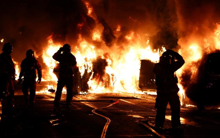 Firefighters attempt to extinguish burning vehicles during clashes between protesters and police