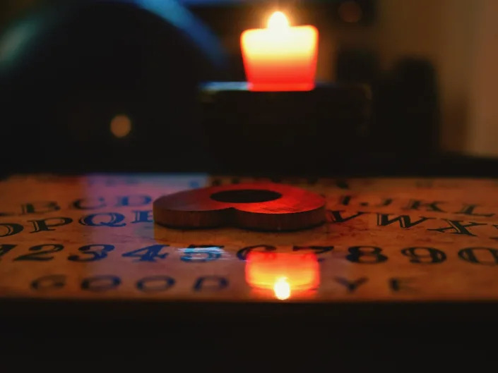Heart Shaped Planchette On Ouija Board By Candle In Darkroom