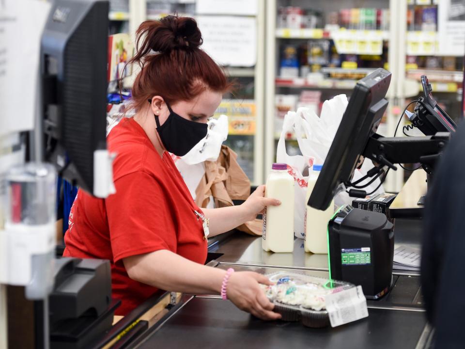 A woman in a face mask and red T-shirt scans groceries at a check-out counter.