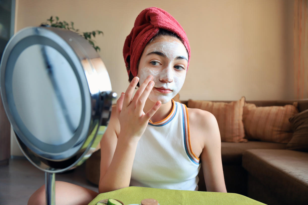 A tween girl applying a white cream to her face in front of a makeup mirror.