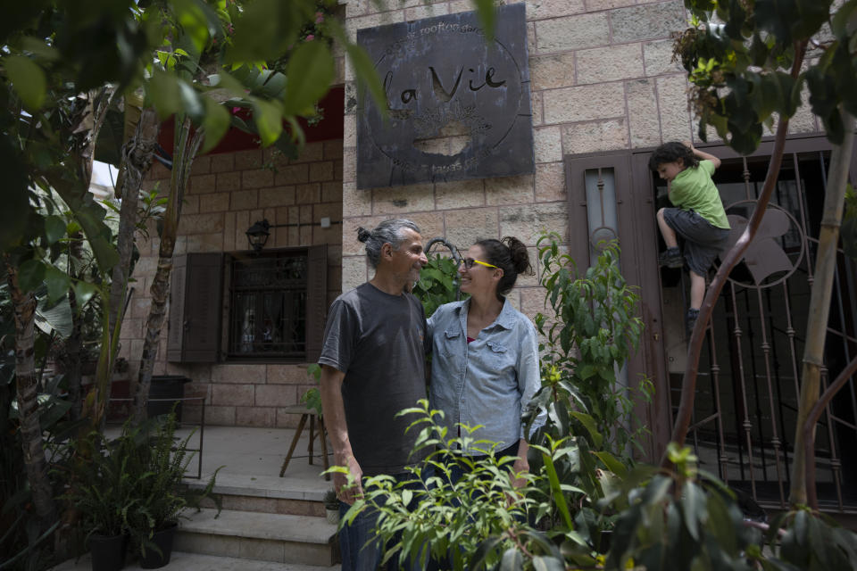 Kenae Totah, 5, right, plays while his parents Morgan Cooper, 41, center and Saleh Totah, right, pose for a photo in front of their restaurant, at the West Bank city of Ramallah, Monday, May 2, 2022. The Israeli military body in charge of civilian affairs in the occupied West Bank has developed a new policy that would heavily regulate entry into the territory. Critics say it extends Israel's nearly 55-year military rule even further into every corner of Palestinian society. It would impose new restrictions on foreigners who work, study or volunteer in the West Bank and those who marry Palestinians. (AP Photo/Nasser Nasser)