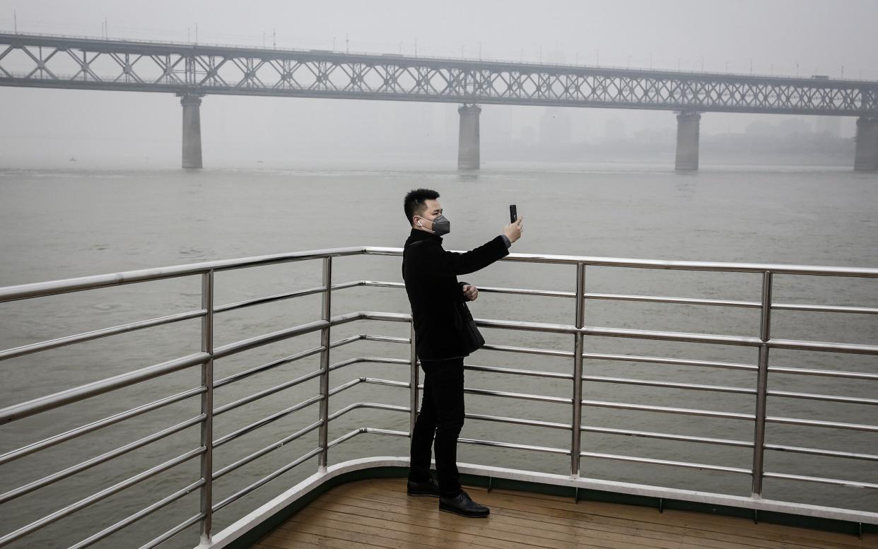 A man wears a mask as he takes a photograph of the Yangtze river, Wuhan - Getty Images AsiaPac