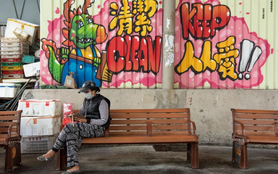 A woman wears a face mask as she sits on a bench in Hong Kong - Rex