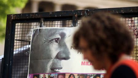 A woman walks past a portrait of Milagro Sala, the leader of the Tupac Amaru social welfare group, as supporters hear Sala's trial in San Salvador de Jujuy, with on charges ranging from intimidation to corruption, on a radio outside a Justice building in Buenos Aires, Argentina, December 28, 2016. REUTERS/Marcos Brindicci