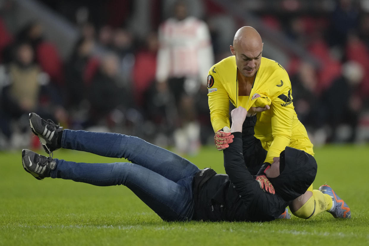 A PSV supporter, on the ground, attacks Sevilla's goalkeeper Marko Dmitrovic during the Europa League playoff second leg soccer match between PSV and Sevilla at the Philips stadium in Eindhoven, Netherlands, Thursday, Feb. 23, 2023. Sevilla won 3-2 on aggregate. (AP Photo/Peter Dejong)