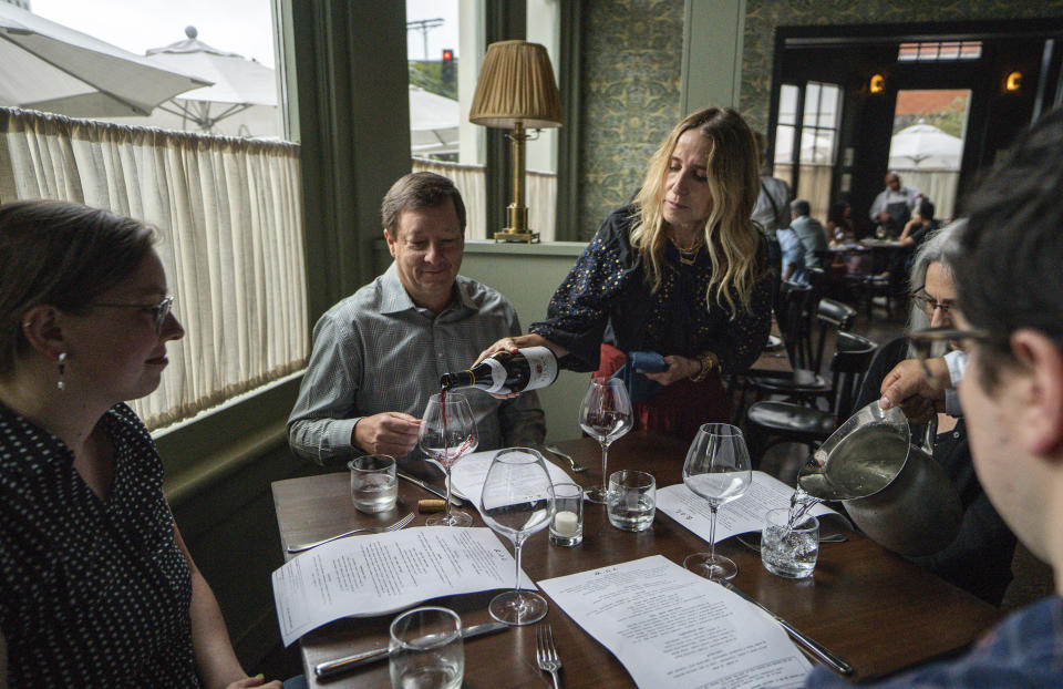 In this Saturday, June 19, 2021, photo, Caroline Styne, owner and wine director at The Lucques Group, serves wine to attorney Alec Nedelman, celebrating early "Father's Day "with his family at the A.O.C. Brentwood restaurant in Los Angeles. Styne has turned away dozens of customers at the company's A.O.C. West Hollywood restaurant because she doesn't have the staff to serve them, leaving seats empty. (AP Photo/Damian Dovarganes)