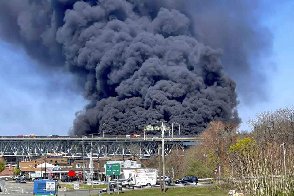 In this photo provided by the Connecticut State Police, massive plumes of smoke rise from a fire resulting from crash involving a fuel truck and a car on the Gold Star Memorial Bridge in Groton, CT., Friday, April 21, 2023. Flames spread to buildings below, causing officials to close Interstate 95 in both directions during the blaze. (Connecticut State Police via AP)