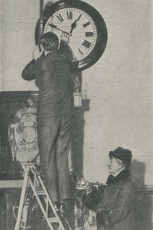 Belville supervising the setting of an office clock