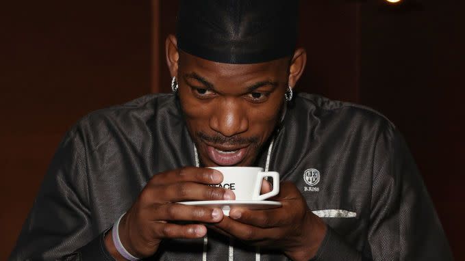 jimmy butler wearing a gray shirt and black durag, holding a white coffee cup hear his mouth
