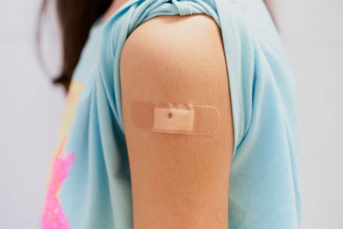 A close-up of a person's upper arm with a bandage applied, indicating they have received a shot or vaccination. The person is wearing a sleeveless shirt