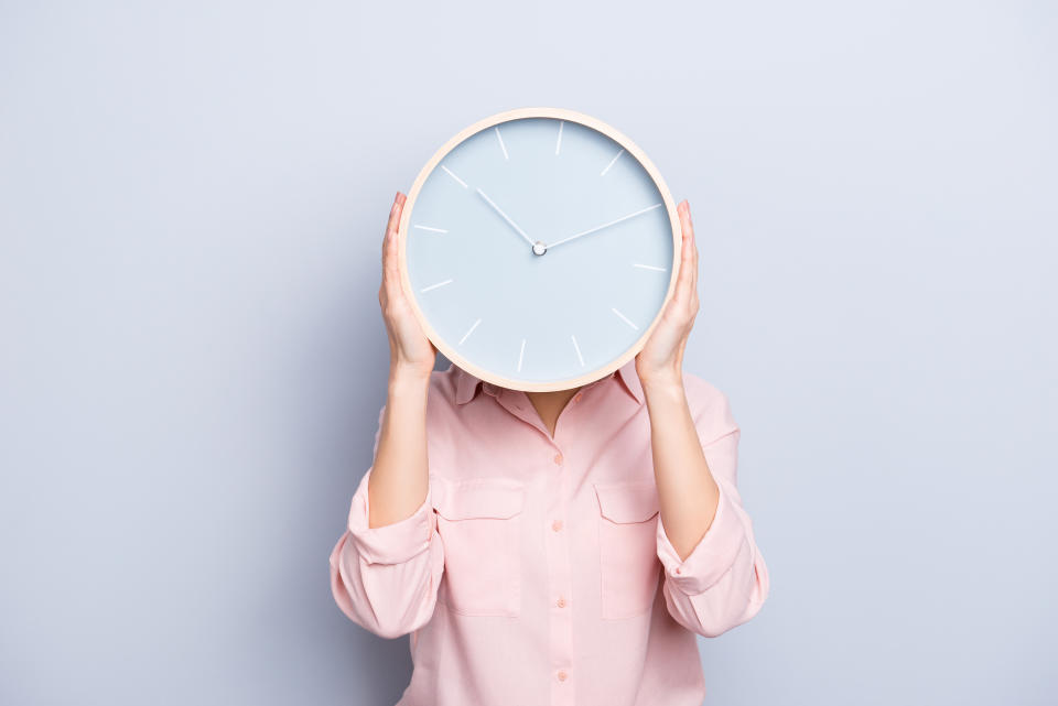 It's 10:10 o'clock. Portrait of charming pretty positive cheerful woman closing covering head face with round clock isolated on grey background