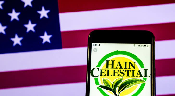 The logo for Hain Celestial (HAIN) displayed on a smartphone screen in front of an American flag.