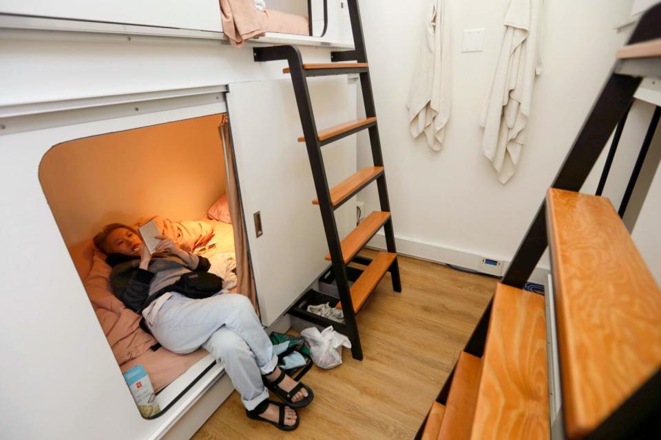 A woman lying on a sleeping pod bed, writing in a journal.