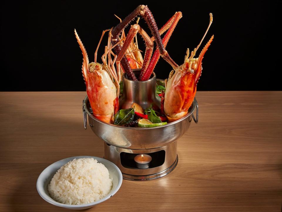 River prawns stick out of a bowl of tom yum soup at Kalaya, with a bowl of white rice served on the side.