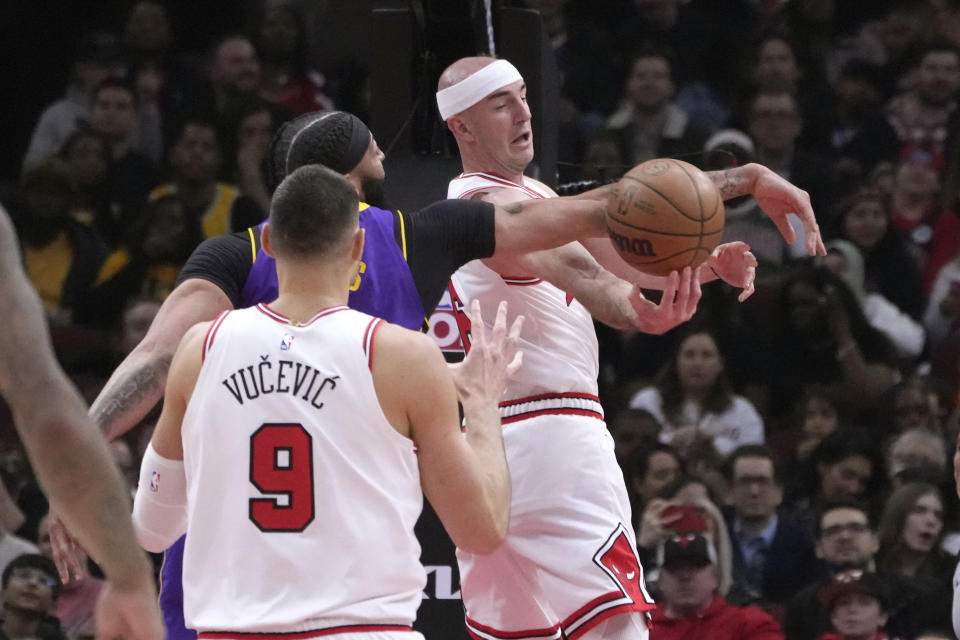 Chicago Bulls' Alex Caruso, right, passes the ball to Nikola Vucevic as Los Angeles Lakers' Anthony Davis defends during the first half of an NBA basketball game, Wednesday, March 29, 2023, in Chicago. (AP Photo/Charles Rex Arbogast)