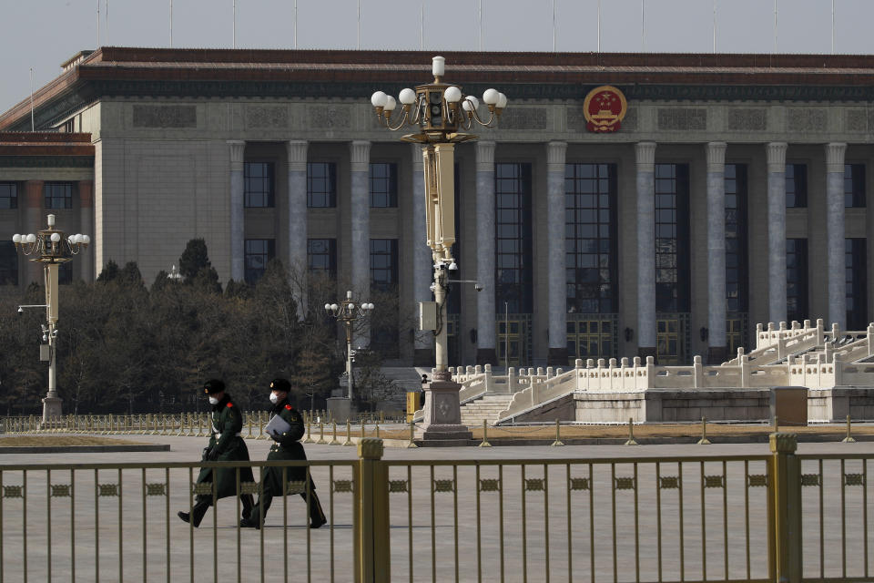 In this Sunday, Feb. 23, 2020, photo, paramilitary policemen wearing protective face masks walk by the empty Tiananmen Square against the back drop of the Great Hall of the People in Beijing. China announced Monday it has postponed its most important political meeting of the year because of the outbreak of the new virus. (AP Photo/Andy Wong)