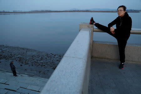 A woman exercises as a man stands at the banks of the Yalu River across from the North Korean town of Sinuiju, in Dandong, China's Liaoning province, March 31, 2017. REUTERS/Damir Sagolj