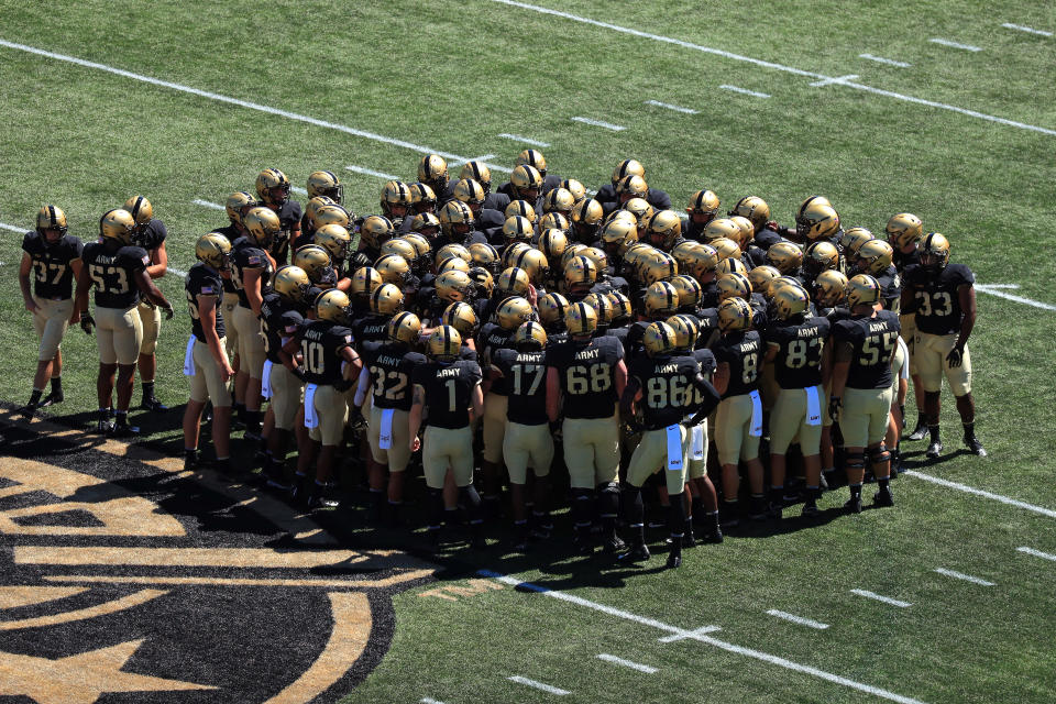 Army football players huddle near the logo on the field.
