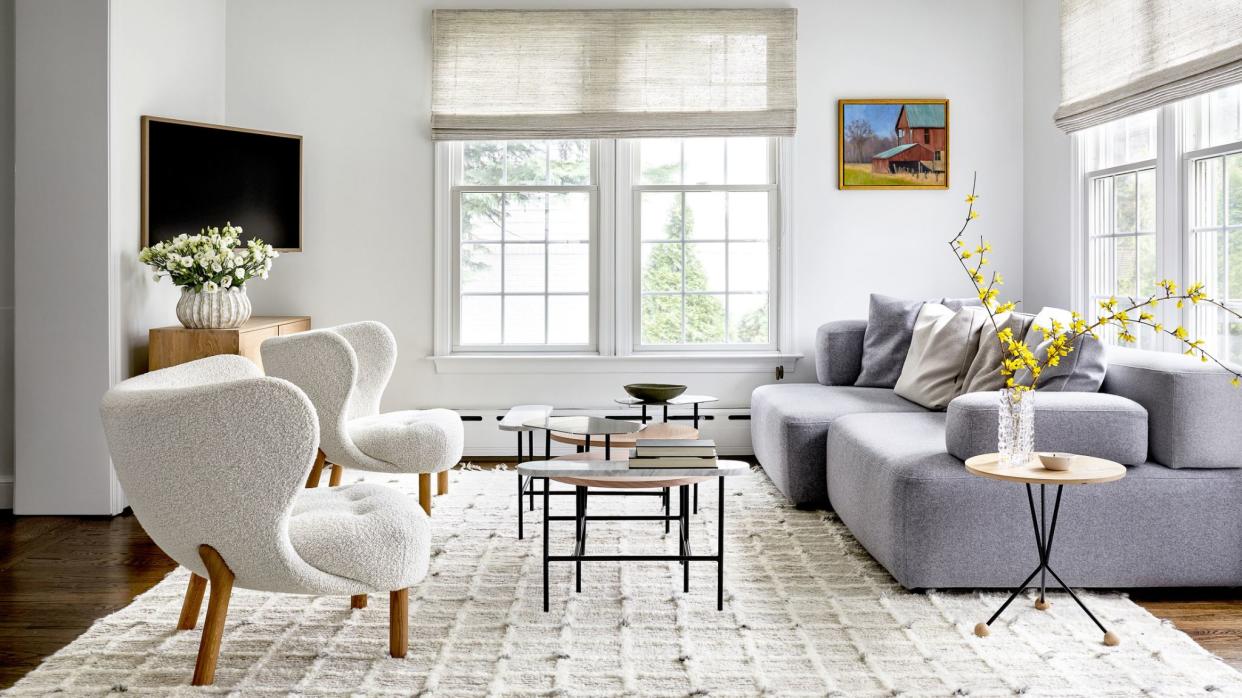  Living room with white walls, two boucle chairs and grey sofa. 